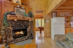 L’intérieur chaleureux d’un chalet avec une cheminée en pierre, une table de billard, un réfrigérateur et une pancarte sur laquelle on peut lire : « SIMPLIFIEZ ».