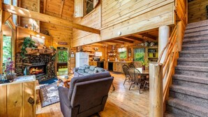 L’intérieur d’un chalet en bois, avec une cheminée, un canapé, une table à manger et un escalier.