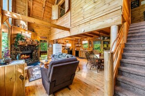 L’intérieur d’un chalet en bois, avec une cheminée, un canapé, une table à manger et un escalier.