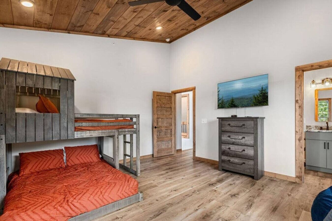 A bedroom with a bunk bed, wooden ceiling, and a dresser with drawers.