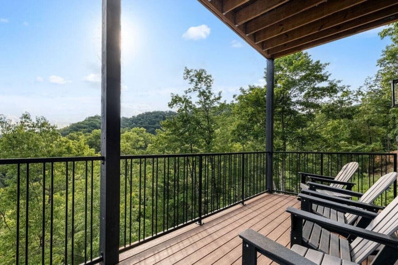 Une terrasse en bois dotée d’une rambarde en métal, offrant une vue sur une zone boisée avec des arbres et des collines.