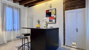 A compact kitchen with a black countertop, two stools, a pineapple, and a vase with flowers. - Mozart Bis (5 min to Rialto's Bridge) (Venecia)