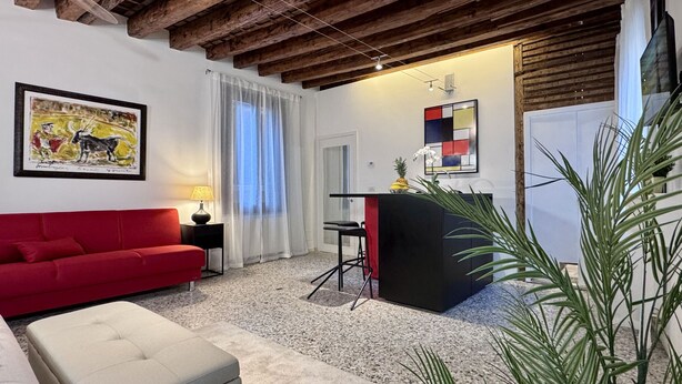 A living room with a red sofa, a small table with a lamp, a black bar counter, and a painting on the wall. - Mozart Bis (5 min to Rialto's Bridge) (Venecia)