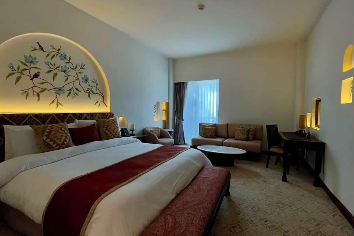 A hotel room with a large bed, a sofa, a small table, and a decorative wall piece.