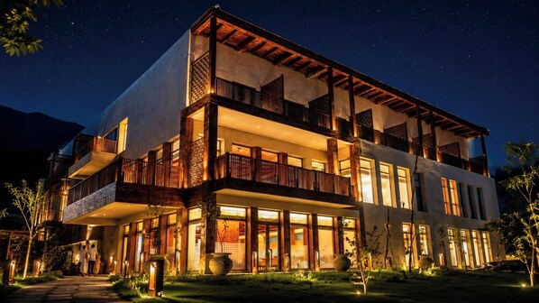 Un hotel de varios pisos con balcones, ventanas amplias y una fachada bien iluminada de noche.