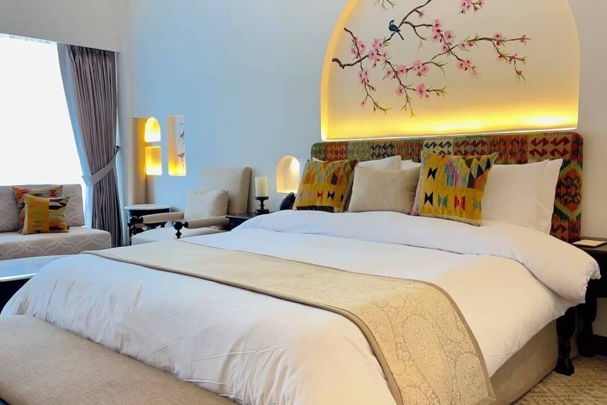 A hotel room with a large bed, a sofa, a desk, and a wall-mounted lamp.