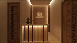 A hallway with a wooden door, a decorative wall with a lotus emblem, and a small plant on a shelf. - Sost Serena Hotel  (Sost)
