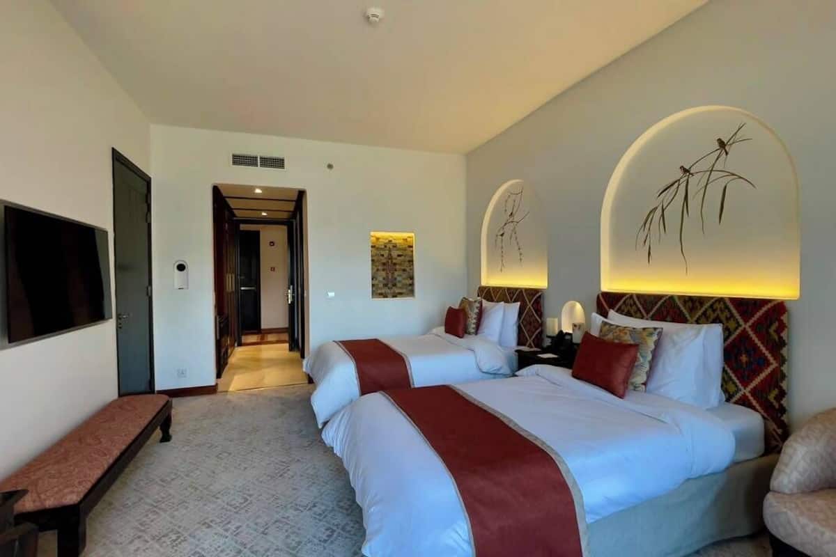 A hotel room with a large bed, a bench, a TV, and a wall-mounted artwork.