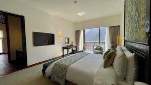 A hotel room with a large bed, a TV, a desk, and a balcony with a mountain view. - Sost Serena Hotel  (Sost)