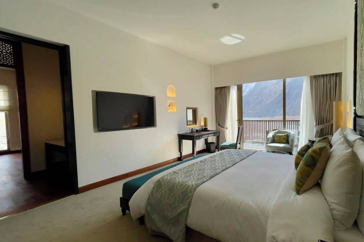 A hotel room with a large bed, a TV, a desk, and a balcony with a mountain view.
