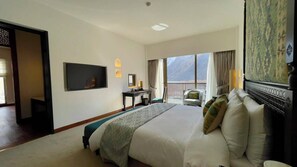 Habitación de hotel con una cama grande, televisión, escritorio y balcón con vistas a la montaña.
