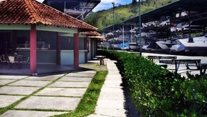 A marina with boats docked, a covered seating area, and a building with a tiled roof. - Angra Convention Hotel (Angra dos Reis)