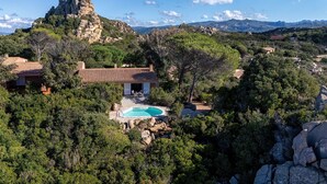 A villa with a swimming pool surrounded by trees and rocky terrain, overlooking a mountainous landscape. - Villa Smeralda New: Sea View, Private Pool and Air Conditioning (Costa Paradiso)