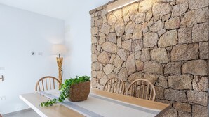 A dining area with a stone wall, wooden table, chairs, and a woven basket with greenery. - Villa Smeralda New: Sea View, Private Pool and Air Conditioning (Costa Paradiso)