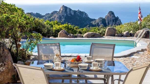 A table set for two with a view of a pool and mountains in the background. - Villa Smeralda New: Sea View, Private Pool and Air Conditioning (Costa Paradiso)