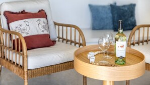 A wicker chair with a white cushion and a red pillow, a round wooden table with a bottle of Aragonese wine, two glasses, and a small decorative item. - Villa Smeralda New: Sea View, Private Pool and Air Conditioning (Costa Paradiso)