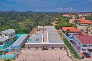 Zona residencial con un edificio moderno, techo plano con paneles solares, piscina y camino de entrada pavimentado.