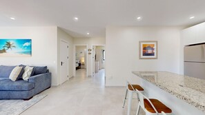 A modern living room with a grey sofa, a kitchen with a granite countertop, and a hallway leading to a bedroom. - Palm Beach Hideaway #8 - New Construction 2Bedrooms 2bathrooms Pool/Rooftop (Noord)