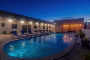 A swimming pool with lounge chairs and a building with multiple doors and windows. - Palm Beach Hideaway #8: Poolfront Corner 2BR with Wraparound Patio (Noord)