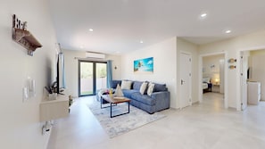 Ein modernes Wohnzimmer mit einem blauen Sofa, einem Couchtisch und einem großen Fenster mit Blick ins Freie.