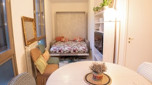 A compact bedroom with a bed, a small table with a plant, a radiator, and a window. - Conti & Moroni House  (Calenzano)