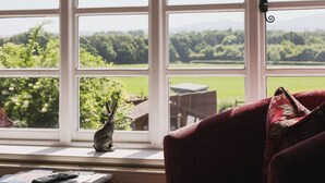 A room with a large window overlooking a green landscape. A red chair is positioned near the window, and a small table with a remote control and papers is visible. - The Haughmond (Upton Magna)