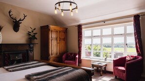 A bedroom with a large bed, a wooden wardrobe, a red armchair, and a view of the outdoors through a window. - The Haughmond (Upton Magna)