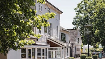 A traditional building with a white facade, large windows, and a small attached structure with a green awning.