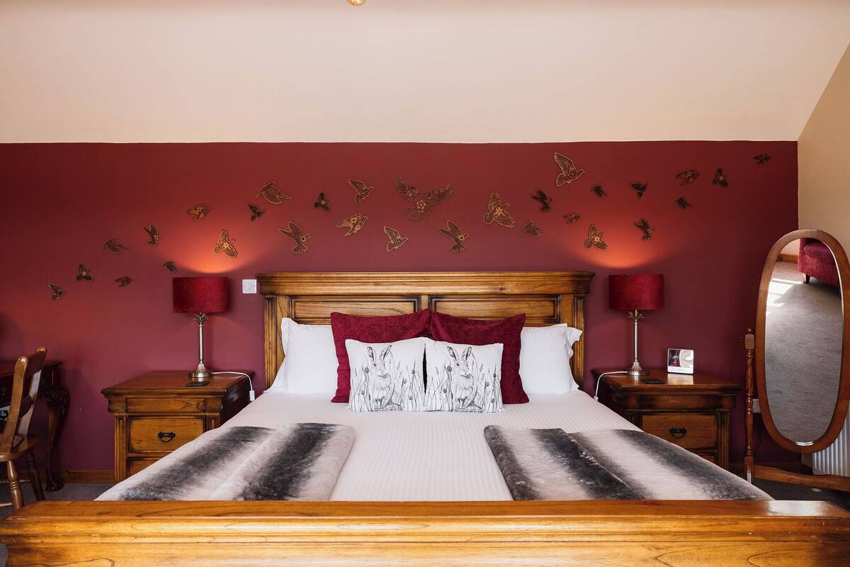 Ein Hotelzimmer mit einem hölzernen Bett, roten Wänden und einem Wandbehang mit Vogelmotiv.