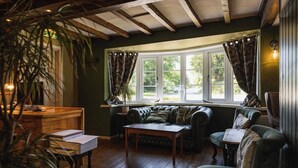 A cozy room with a green sofa, a wooden table, and a window with curtains. - The Haughmond (Upton Magna)