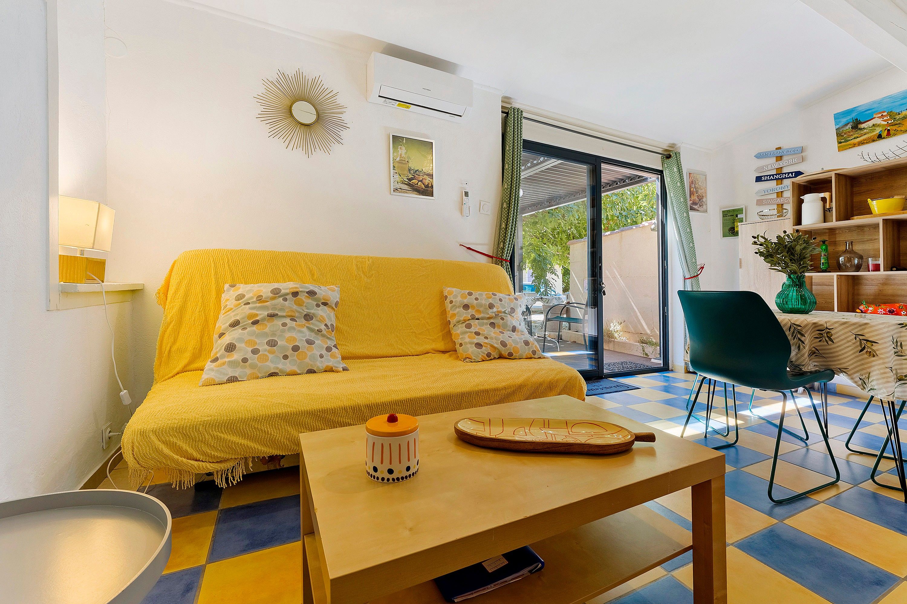 Una sala de estar con un sofá amarillo, una mesita y un comedor con una silla.