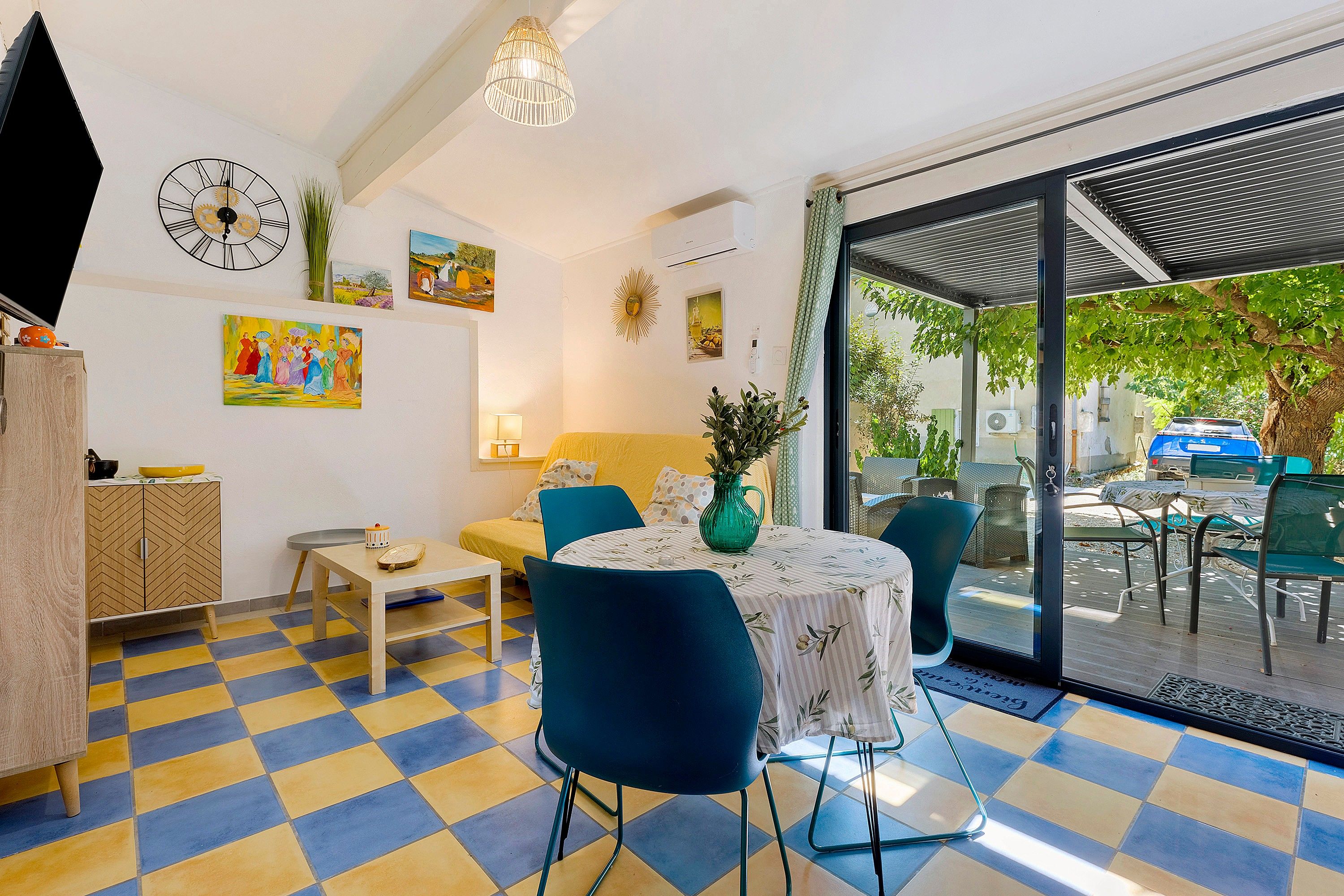 Een kamer met een zwart-wit geruite vloer, een tafel met stoelen, een bank en een groot raam met uitzicht op de omgeving.