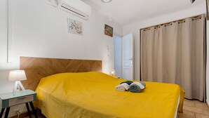 Ein Hotelzimmer mit einem Bett, einem Nachttisch mit Lampe, einer Tür mit Vorhang und einer Klimaanlage an der Wand.