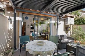 An outdoor patio with a round table, chairs, and a glass door leading to an interior space. - Gîte Les Garrigues – Modern Comfort Near Les Baux-de-Provence, Sleeps 3 (Mouriès)