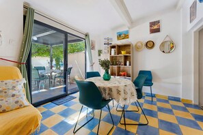 A dining area with a table set for two, chairs, a vase, and a bookshelf with various items. - Gîte Les Garrigues – Modern Comfort Near Les Baux-de-Provence, Sleeps 3 (Mouriès)