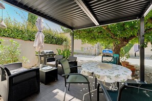 An outdoor patio with wicker furniture, a table with a patterned tablecloth, and a grill. - Gîte Les Garrigues – Modern Comfort Near Les Baux-de-Provence, Sleeps 3 (Mouriès)
