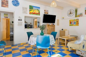 A dining area with a checkered floor, a table with chairs, a television, and various wall decorations. - Gîte Les Garrigues – Modern Comfort Near Les Baux-de-Provence, Sleeps 3 (Mouriès)