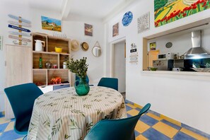 A dining area with a round table, chairs, a vase with greenery, and a wall with various decorations including a clock and a sign with city names. - Gîte Les Garrigues – Modern Comfort Near Les Baux-de-Provence, Sleeps 3 (Mouriès)