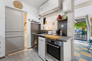 A compact kitchen with a dishwasher, oven, and a coffee maker. - Gîte Les Garrigues – Modern Comfort Near Les Baux-de-Provence, Sleeps 3 (Mouriès)