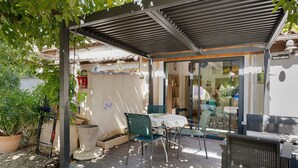 Ein Außenbereich mit Sitzgelegenheiten, einem Tisch, Stühlen, einer Pergola und Kübelpflanzen.