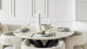 A dining table with white plates, glasses, and a vase, surrounded by beige chairs. - 2BR M Huge Terrace Direct Canal Access (Dubai)