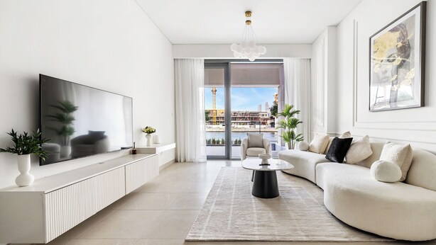 A modern living room with a large flat-screen TV, a sofa, a coffee table, and a view of a cityscape through large windows. - 2BR M Huge Terrace Direct Canal Access (Dubai)