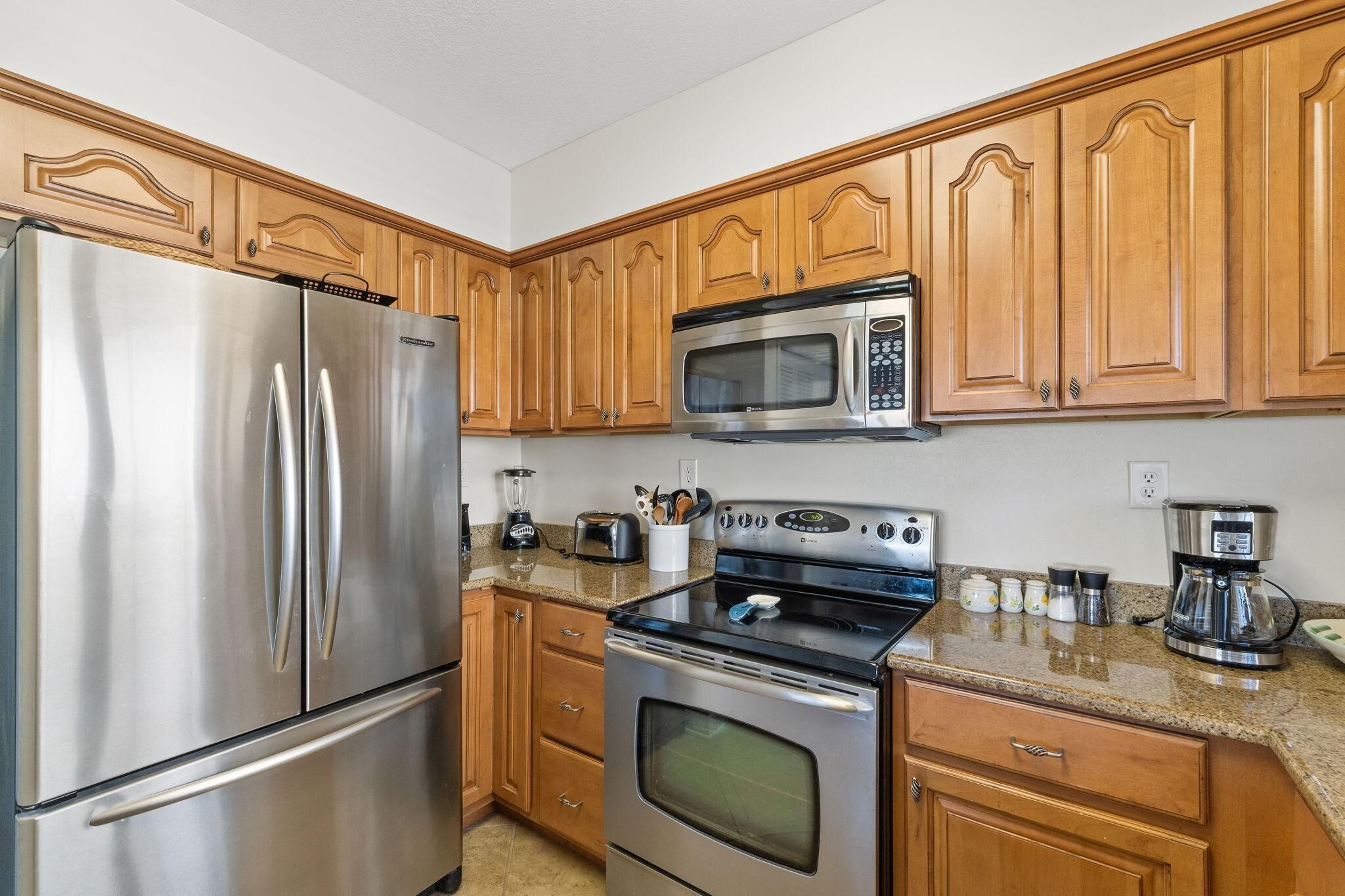 Una cocina con armarios de madera, un refrigerador de acero inoxidable, un microondas, un horno y una cafetera.