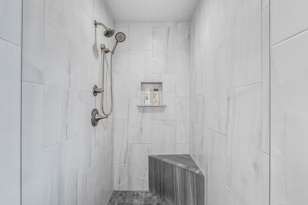 A narrow shower with white marble walls and a built-in shelf holding toiletries.