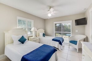 A hotel room with two beds, a ceiling fan, a TV, and a window with blinds. - Barefoot Bliss - Heated Pool, Walk to the Beach, Ping Pong (St. Augustine)