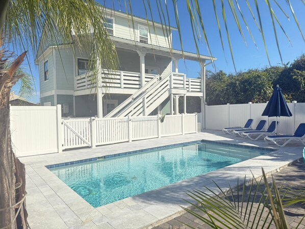 A pool with a white fence, a two-story building, and lounge chairs. - Barefoot Bliss - Heated Pool, Walk to the Beach, Ping Pong (St. Augustine)