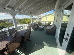 A covered outdoor patio with wicker furniture, a wooden table, and a glass door leading to a house. - Barefoot Bliss - Heated Pool, Walk to the Beach, Ping Pong (St. Augustine)