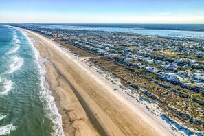 Luchtbeeld van een kustgebied met woonhuizen, een lang zandstrand en helder uitzicht op de oceaan.