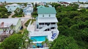 Uma casa de dois andares com piscina, rodeada por vegetação exuberante e uma praia ao fundo.