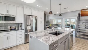 Uma cozinha moderna com armários brancos, eletrodomésticos de aço inoxidável e bancada de mármore.